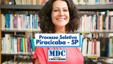 Mulher sorridente de cabelos castanhos e cacheados veste uma blusa rosa e está em pé em frente a uma estante de livros em uma biblioteca. No centro da imagem, há uma faixa com os dizeres “Processo Seletivo Piracicaba - SP” e, abaixo, o logotipo da MDC Concursos. A imagem transmite um ambiente educacional e promove um processo seletivo na cidade de Piracicaba, em São Paulo.