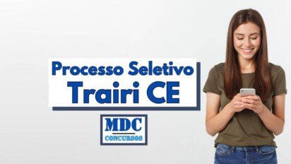 Imagem com fundo claro mostrando uma jovem sorridente de cabelos longos castanhos, vestindo camiseta verde-oliva e jeans, olhando para o celular nas mãos. Ao lado esquerdo da imagem está o texto “Processo Seletivo Trairi CE” em letras grandes azul-escuro com sombra, e abaixo o logotipo da MDC Concursos, indicando a divulgação de um novo processo seletivo na cidade de Trairi no Ceará