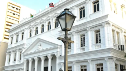 Fachada branca do fórum sede do estágio TJMA com bandeiras hasteadas e poste antigo