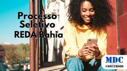 Mulher jovem com cabelo cacheado e pele morena sentada em uma escada ao ar livre, usando moletom amarelo e calça jeans, sorrindo enquanto olha para o celular. O fundo mostra um céu azul, um corrimão metálico enferrujado e prédios ao longe - REDA Bahia abre 22 Vagas com salários de até R$ 3.373 em Processo Seletivo