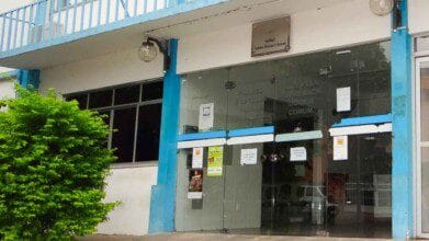 Processos Seletivos 6 Entrada da Prefeitura Municipal de Brumado com portas de vidro e avisos afixados, fachada branca com detalhes em azul.