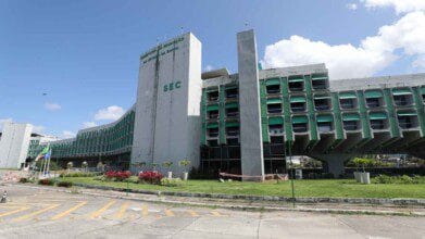 Processos Seletivos 3 Prédio da Secretaria da Educação do Estado da Bahia (SEC), com fachada cinza e janelas verdes, em dia ensolarado com céu azul.