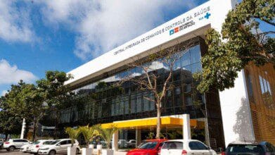 Processos Seletivos 5 Fachada envidraçada da Central Integrada de Comando e Controle da Saúde da Bahia com carros estacionados em frente e árvores ao redor.