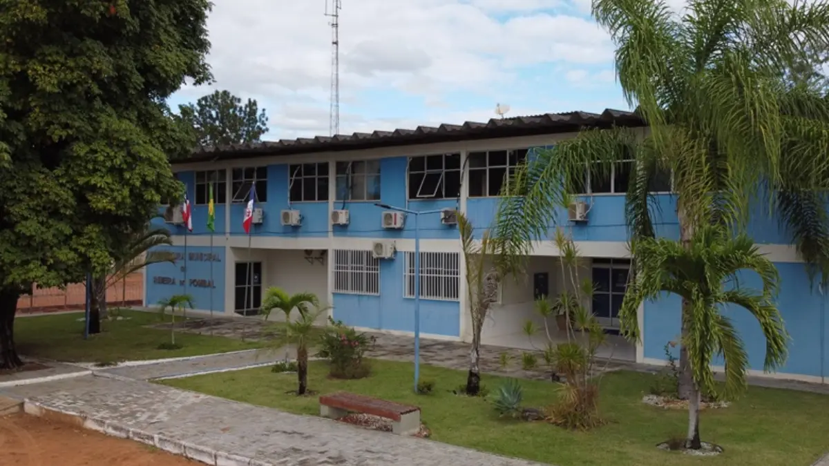 Resultado processo seletivo Ribeira do Pombal BA: lista preliminar já está disponível 1 Fachada do prédio da Prefeitura de Ribeira do Pombal com dois pavimentos, pintura azul e branca, jardim com palmeiras e bandeiras oficiais na entrada, referente ao processo seletivo Ribeira do Pombal BA