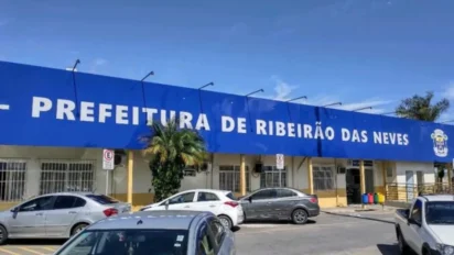 Fachada da Prefeitura de Ribeirão das Neves com placa azul exibindo o nome da instituição, carros estacionados em frente ao prédio e céu azul ao fundo. Foto: Divulgação/Prefeitura de Ribeirão das Neves-MG