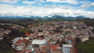Vista aérea da cidade de Rodeiro-MG com casas, prédios e montanhas ao fundo sob céu parcialmente nublado. Foto: Divulgação/Prefeitura de Rodeiro-MG