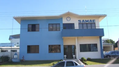 Fachada da sede do SAMAE em Campos Novos, um prédio de dois andares nas cores azul e bege, com o logotipo e o nome da autarquia em destaque na parte superior. Foto: Deyvid Setti e Eloy Olindo Setti/Wikipédia