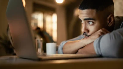 Homem observa a tela de um notebook com expressão pensativa, apoiando o queixo nos braços em um ambiente interno iluminado. Foto: Drazen Zigic/Freepik