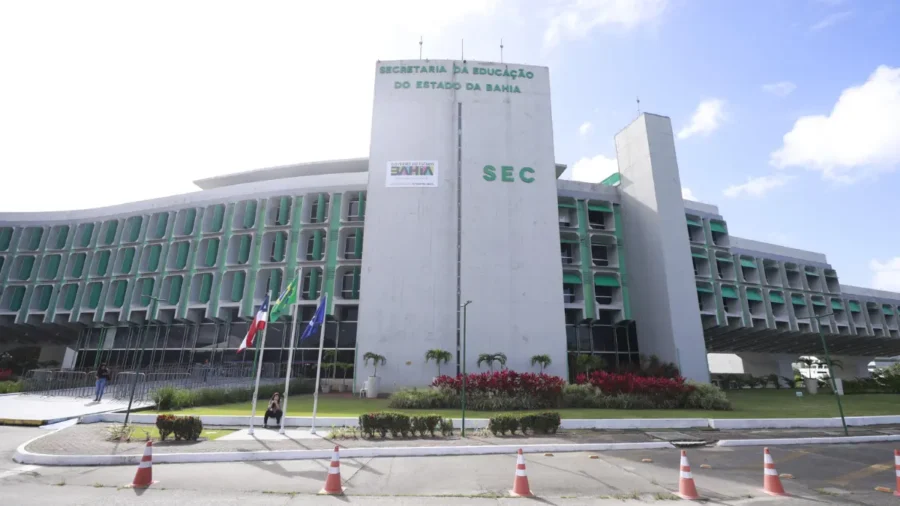 fachada da Secretaria da Educação do Estado da Bahia (SEC-BA), sede do REDA SEC BA, com prédio moderno em tons de branco e verde, bandeiras hasteadas e jardim frontal