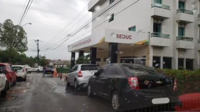 Fachada do prédio da Secretaria de Estado da Educação do Maranhão (SEDUC) em um dia chuvoso, com carros estacionados à frente e identificação na marquise branca.