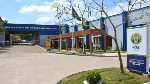 SEE Acre lança processo seletivo com 256 vagas e salários de até R$ 3.483,69 4 Fachada da Secretaria de Estado de Educação, Cultura e Esportes do Acre com letreiro azul, bandeiras hasteadas e entrada principal com cobertura de madeira. Foto: Divulgação/SEE Acre