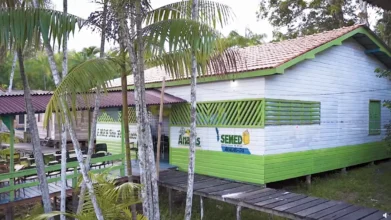 Prédio escolar de madeira com pintura verde e branca, cercado por palmeiras, com passarela de madeira e logotipo da SEMED Anajás-PA na fachada. Foto: Divulgação/Prefeitura de Anajás-PA