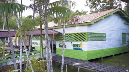 Prédio escolar de madeira com pintura verde e branca, cercado por palmeiras, com passarela de madeira e logotipo da SEMED Anajás-PA na fachada. Foto: Divulgação/Prefeitura de Anajás-PA