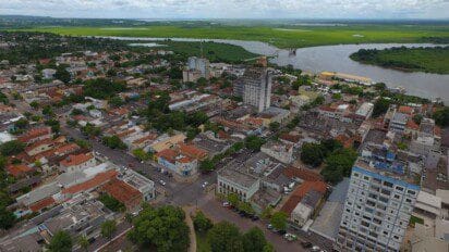 Vista aérea da cidade de Corumbá com prédios, casas, ruas arborizadas e o rio Paraguai ao fundo.