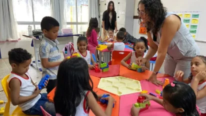 Professora auxilia crianças em sala de aula enquanto alunos pequenos brincam e montam blocos coloridos em mesas coletivas. Foto: Divulgação/Prefeitura de Marabá