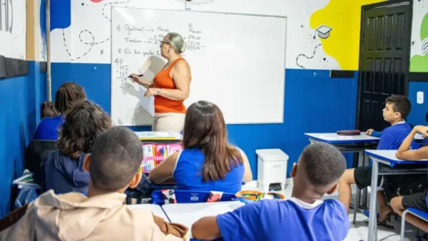 Professora escreve no quadro enquanto alunos sentados observam em uma sala de aula colorida. Foto: Divulgação/Prefeitura de São Pedro da Aldeia-RJ