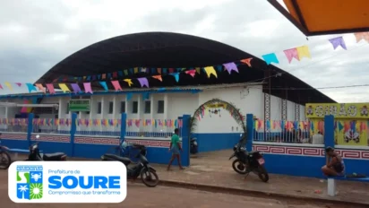 Fachada de escola municipal em Soure decorada com bandeirinhas coloridas, com motos estacionadas e pessoas circulando em frente ao prédio. Foto: Divulgação/Prefeitura de Soure-PA