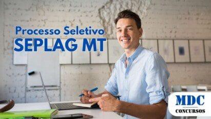 Jovem sorridente com camisa azul clara sentado em um espaço moderno de coworking, segurando uma caneta e um caderno, com um laptop à sua frente. O ambiente tem parede rústica, quadros e um quadro branco ao fundo, além de mesas e cadeiras brancas - SEPLAG MT abre 44 vagas para Analista de TI com salários de até R$ 18.585