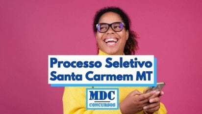 Mulher negra sorridente usando óculos de armação grossa e blusa amarela aparece segurando um celular contra um fundo rosa vibrante. Sobre a imagem, há uma faixa com o texto “Processo Seletivo Santa Carmem MT” em letras grandes e azul-escuras. Abaixo, o logotipo “MDC Concursos” está centralizado em destaque com moldura azul e letras maiúsculas