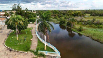 Vista aérea de parque urbano com equipamentos de ginástica, palmeiras e calçadão à margem de um rio em Santa Rita de Cássia, BA