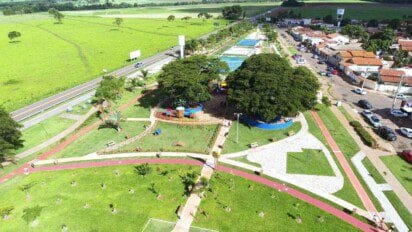 Vista aérea de parque urbano em Santo Antônio de Goiás com área verde, pista de caminhada, playground, árvores e piscina ao lado de avenida e residências
