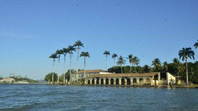 Processos Seletivos 2 Vista de construção histórica à beira-mar em São Francisco do Conde cercada por palmeiras e céu azul claro. Foto: Divulgação/Prefeitura de São Francisco do Conde-BA