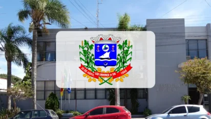 Fachada do prédio da Prefeitura Municipal de São Lourenço do Sul, no Rio Grande do Sul, com o brasão de armas da cidade centralizado em destaque sobre a imagem. No registro, é possível ver a entrada do edifício cinza, palmeiras e carros estacionados em frente sob um céu azul claro. Foto: Montagem MDC Concursos/Divulgação/Google Maps (J. Fauri)
