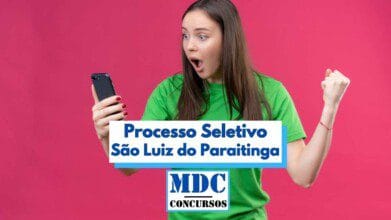 Processos Seletivos 4 Mulher jovem de camiseta verde, com expressão de surpresa e felicidade, segura um celular e comemora com o punho cerrado diante de um fundo rosa vibrante. Ao centro da imagem, há uma faixa com os dizeres “Processo Seletivo São Luiz do Paraitinga” em destaque azul, acompanhada do logotipo “MDC Concursos” na parte inferior, indicando uma oportunidade de concurso público.