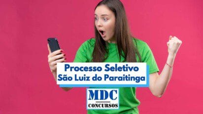 Mulher jovem de camiseta verde, com expressão de surpresa e felicidade, segura um celular e comemora com o punho cerrado diante de um fundo rosa vibrante. Ao centro da imagem, há uma faixa com os dizeres “Processo Seletivo São Luiz do Paraitinga” em destaque azul, acompanhada do logotipo “MDC Concursos” na parte inferior, indicando uma oportunidade de concurso público.