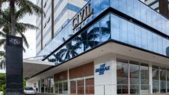 Fachada envidraçada do prédio Civil Towers com a unidade do Sebrae BA no térreo, identificada por logotipo azul na parede branca e entrada com portas de vidro.