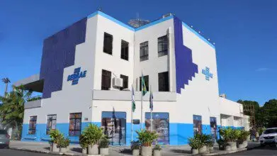 Fachada do prédio do Sebrae RR em Boa Vista, com paredes brancas, detalhes em azul e bandeiras na entrada.