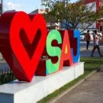 Escultura urbana com coração vermelho e as letras SAJ coloridas em Santo Antônio de Jesus-BA, com pessoas e comércios ao fundo. Foto: Divulgação/Santo Antônio de Jesus-BA