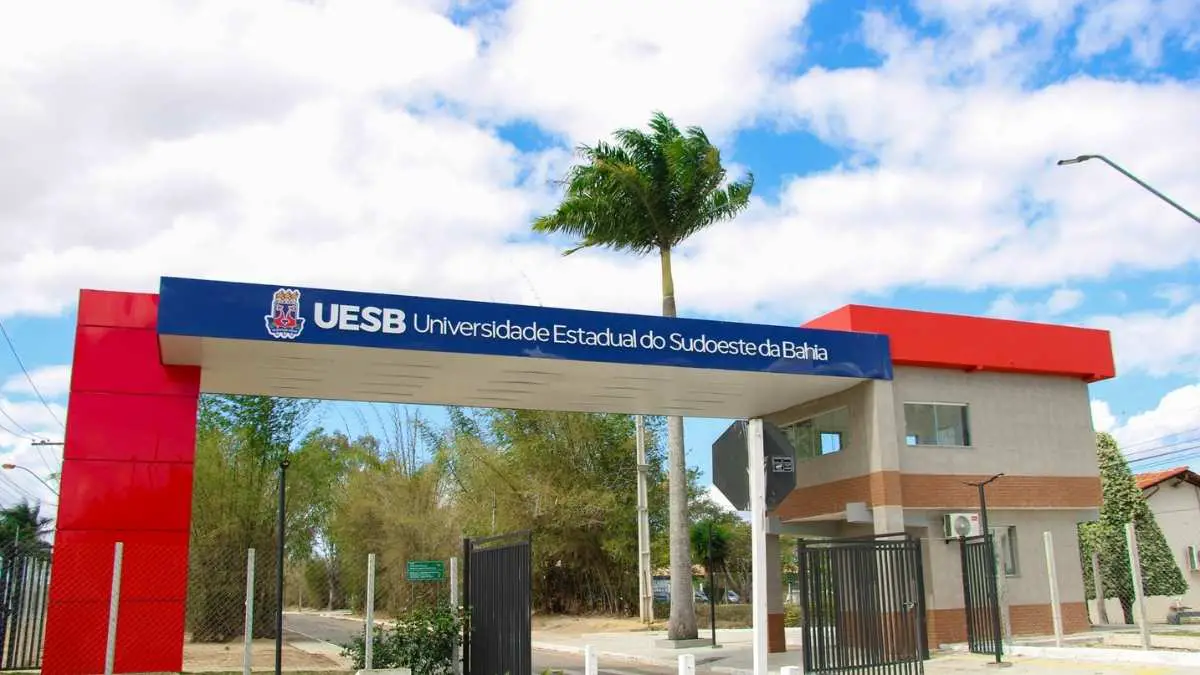 Seleção REDA: UESB abre 30 vagas imediatas de até R$ 3,6 mil 6 Entrada principal da Universidade Estadual do Sudoeste da Bahia (UESB) com portaria, portão aberto, placa azul com o nome da universidade, céu parcialmente nublado e palmeira ao fundo. Foto: Divulgação/Ascom-Uesb
