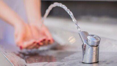 Torneira de água potável jorrando em arco com mãos em segundo plano para se lavar.