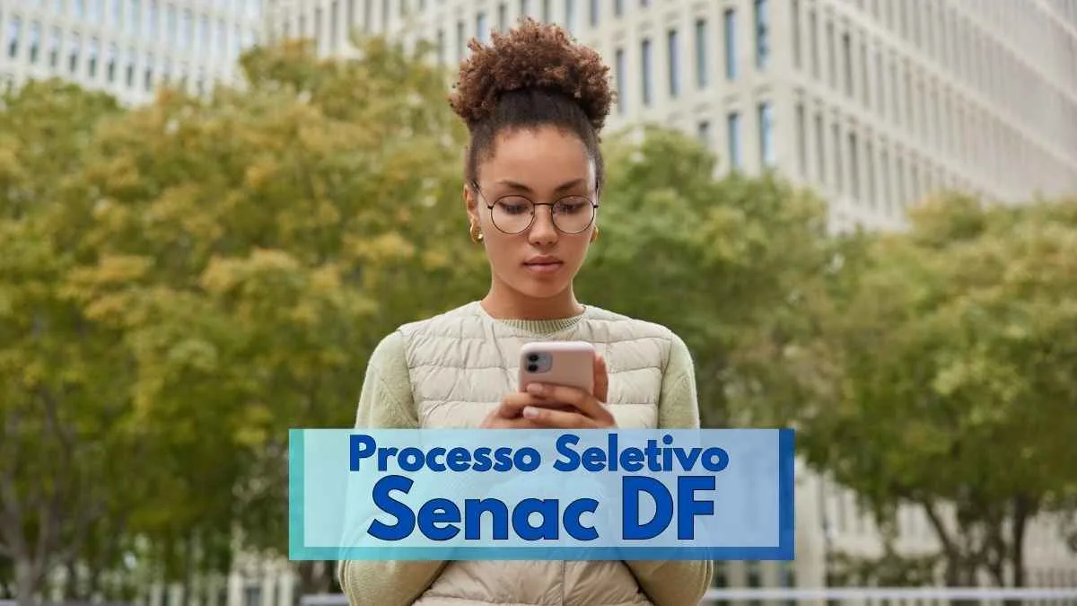 Senac DF lança seleção com salários de até R$ 5.493,97 1 Mulher jovem de pele morena e cabelo crespo preso em coque, usando óculos redondos e colete claro, olha atentamente para um celular. Ela está ao ar livre, com árvores ao fundo e edifícios modernos ao redor. Na imagem, há um banner em destaque com os dizeres "Processo Seletivo Senac DF", indicando oportunidade profissional. O clima parece ameno, típico de meia-estação.