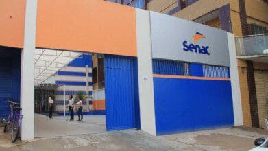 Fachada de unidade do Senac com portão azul e pessoas conversando na entrada.