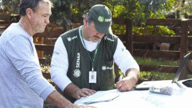 Processos Seletivos 4 Técnico do SENAR RS preenche documentos ao ar livre enquanto conversa com produtor rural.