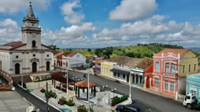 Vista aérea do centro de Serraria/PB com igreja histórica, praça com quiosques, rua asfaltada e casarios coloridos sob céu azul com nuvens. Foto: Divulgação/Prefeitura de Serraria-PB