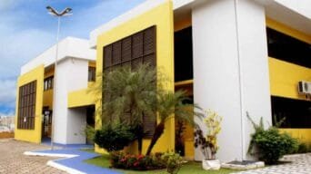 Fachada do Sesc Esplanada em Porto Velho, com paredes amarelas e brancas, janelas com persianas escuras, jardim com palmeiras e calçada com faixa azul.