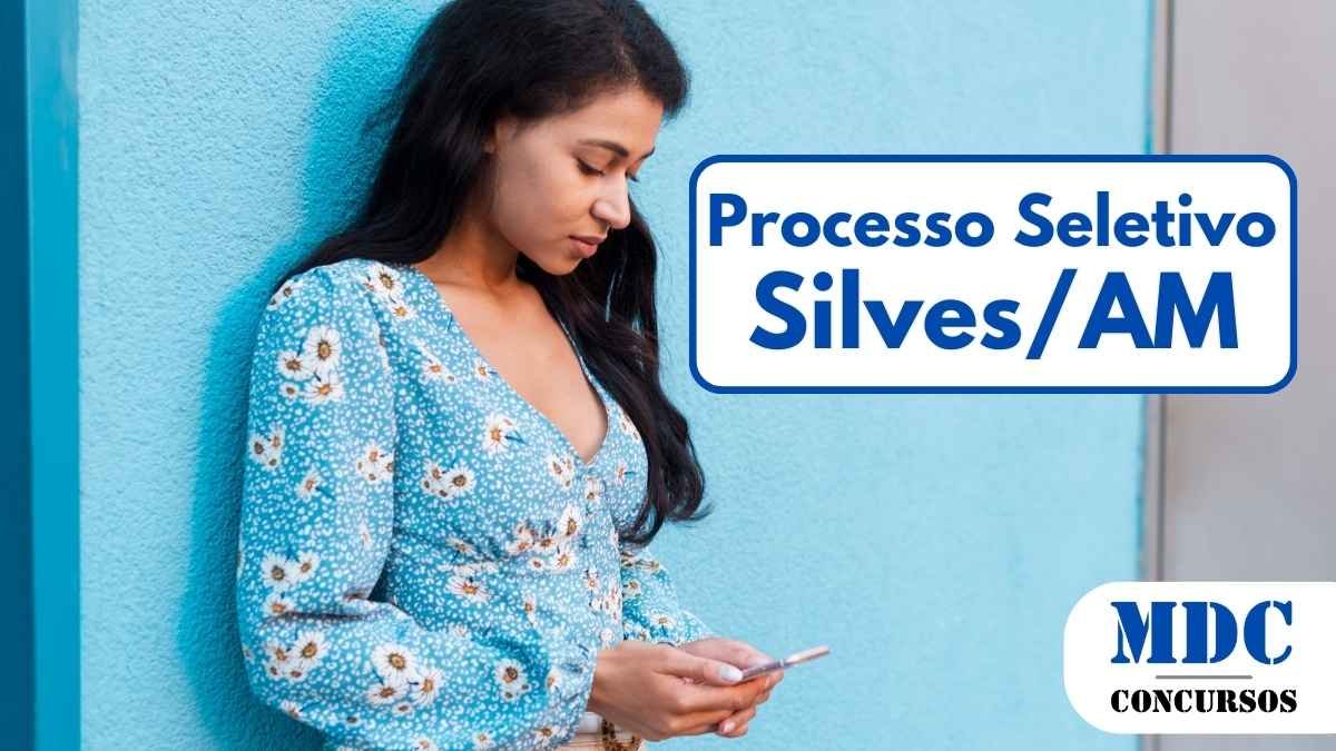Mulher jovem com cabelo longo e escuro, vestindo uma blusa azul florida e calça bege, encostada em uma parede azul enquanto olha para o celular - Silves AM abre 27 vagas com salários de até R$ 6 mil em Processo Seletivo