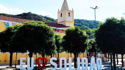 Praça central de Solidão com letreiro “Eu amo Solidão”, árvores alinhadas, igreja ao fundo e morros verdes compondo a paisagem urbana do município. Foto: Divulgação/Google Maps (Marcos Estrela)