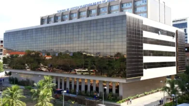TJRJ lança concurso público com salários de até R$ 12.924,41 4 Fachada espelhada do prédio do Tribunal de Justiça do Estado do Rio de Janeiro com árvores e ônibus refletidos nas janelas. Foto: Divulgação/TJRJ