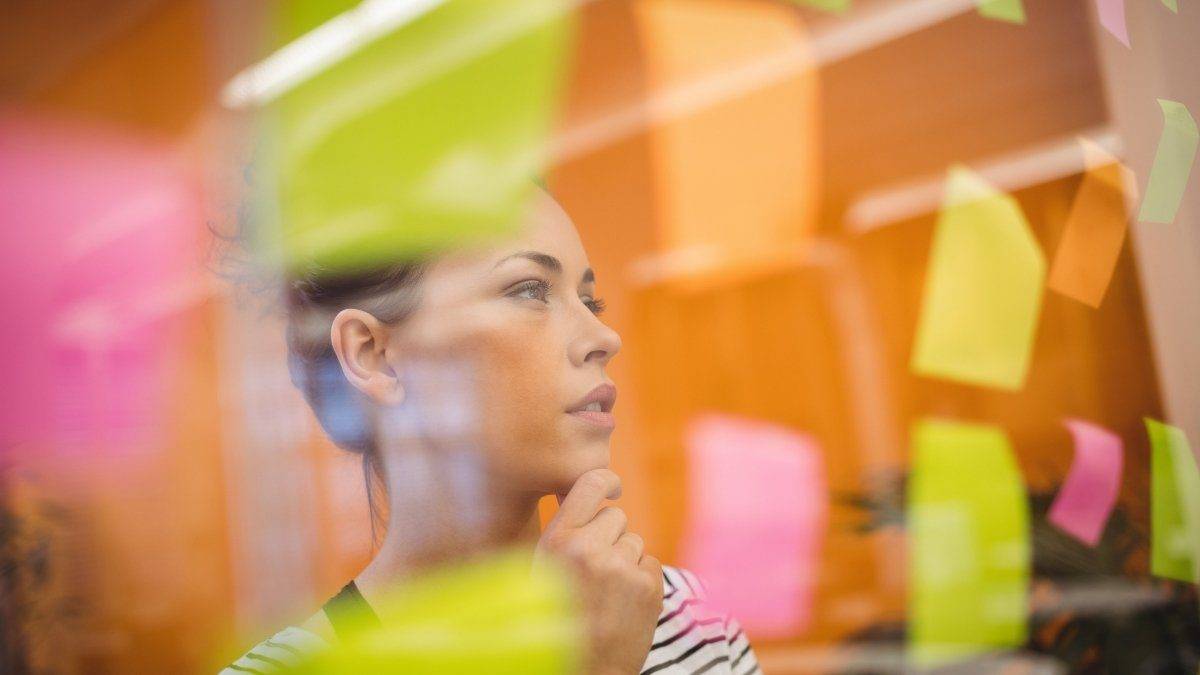 Como estudar após o trabalho: estratégias para quem tem pouco tempo 2 Mulher pensativa olhando para post-its coloridos colados em um vidro. Foto: peoplecreations/Freepik