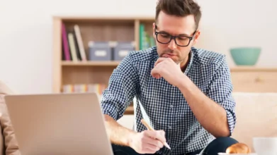 Telebras abre concurso com 930 vagas e salários de R$ 11.680,78 5 Homem usando óculos trabalha concentrado em um notebook enquanto faz anotações em um ambiente doméstico. Foto: gpointstudio/Freepik