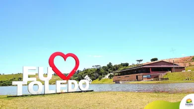 Paisagem de Toledo-MG com letreiro “Eu amo Toledo” à beira de um lago e prédio ao fundo em área verde sob céu azul. Foto: Divulgação/Prefeitura de Toledo-MG