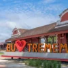 Fachada da antiga estação ferroviária de Tremembé, com prédio histórico em tons de vermelho e branco, uma locomotiva a vapor à esquerda e um letreiro turístico colorido escrito Eu amo Tremembé em destaque.