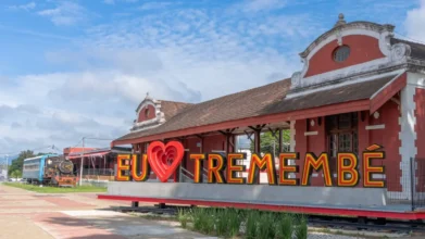 Fachada da antiga estação ferroviária de Tremembé, com prédio histórico em tons de vermelho e branco, uma locomotiva a vapor à esquerda e um letreiro turístico colorido escrito Eu amo Tremembé em destaque.