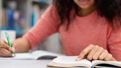 Pessoa estudando em uma mesa com livros abertos, escrevendo e lendo atentamente. Foto: Freepik