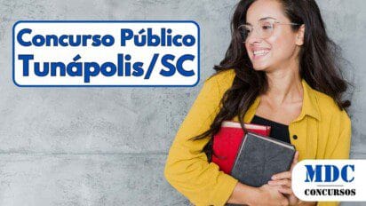 Mulher sorridente com óculos transparentes, usando camisa amarela e segurando dois livros, um vermelho e um preto, em frente a uma parede cinza - Tunápolis (SC) oferece remuneração de até R$ 5,1 mil em Concurso Público