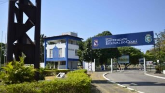 Entrada do campus Itaperi da Universidade Estadual do Ceará com placa de boas-vindas, guarita azul e branca e área arborizada ao fundo